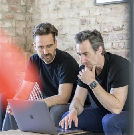 2 männliche Mitarbeiter sitzen auf Sofa und arbeitet an Laptop